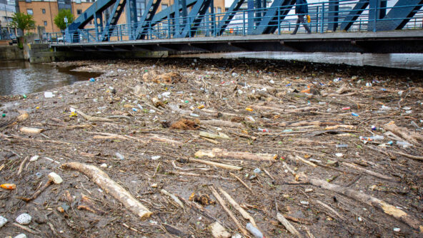 Debris floating in the Water of Leith in front of a bridge.