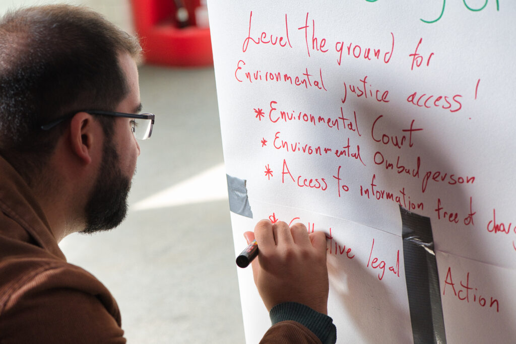 Participant at the Environmental Rights Summit 2023 writing on paper: 'Level the ground for environmental justice access! Environmental court, environmental ombudsperson, access to information free of charge'